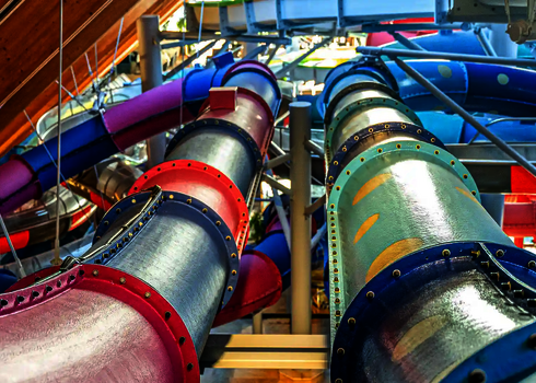 Blick auf mehrere bunte Wasserrutschen in einer großen, überdachten Wassererlebniswelt.