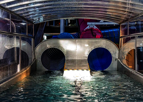 Zwei Wasserrutschenausläufe enden in einem Wasserbecken unter einem transparenten Dach.