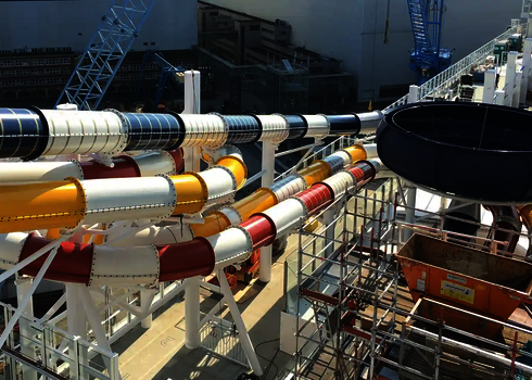 Mehrere bunte Wasserrutschen schlängeln sich über das Schiff in einem Werftbereich.