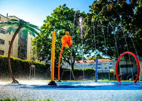 Wasserspielplatz mit spritzenden Wie-Spray Elementen vor Hotelanlage.