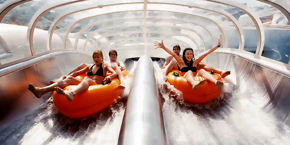 Zwei Teams rutschen auf zwei parallel verlaufenden Bahnen auf orangenen Reifen die Raft Racer Wasserrutsche hinab.