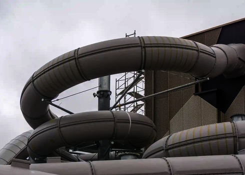 Blick von außen auf ein Gebäude, aus dem eine weiße Wasserrutsche herauskommt.