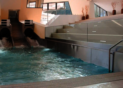Two black tube slides lead into a wide stainless steel pool with a water channel.