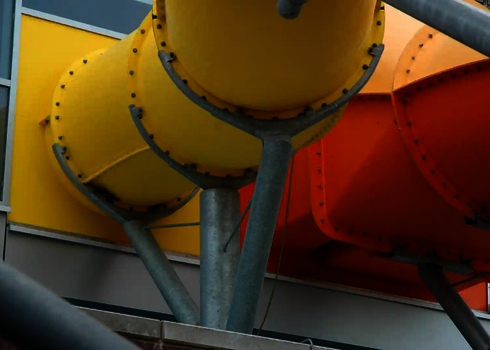 Gelbe und orangefarbene Wasserrutschen verlassen buntes Gebäude mit Trägern.