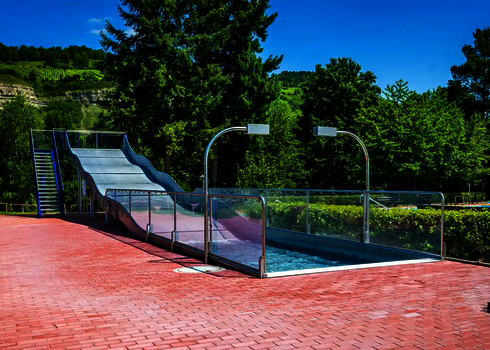 Eine Breitwellenrutsche mit Auslaufbecken vor einer grünen Landschaftskulisse.