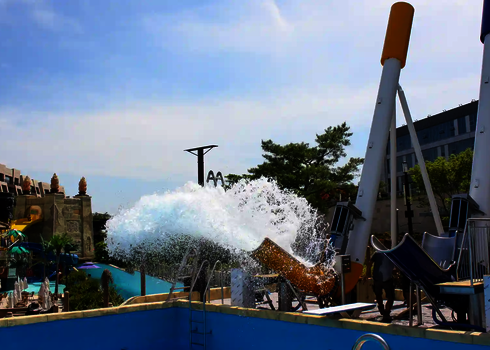 Gelber und blauer Cannonball vor einem Schwimmbecken, mit blauem Himmel im Hintergrund.
