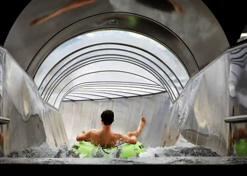 Ein Mann fährt auf einem grünen Reifen durch eine transparente Rutsche mit Tageslichteinfall.