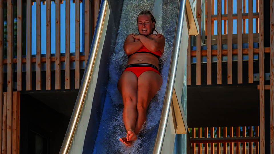 Eine Frau rutscht in Rückenlage durch eine steile Freifallrutsche ins Wasserbecken.