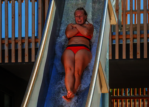 Eine Frau rutscht in Rückenlage durch eine steile Freifallrutsche ins Wasserbecken.