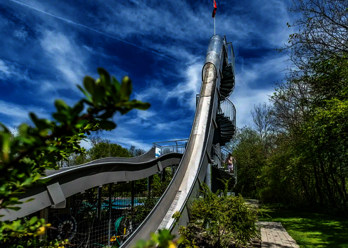 Steile Freifallrutsche mit Wendeltreppe im Freibad, im Hintergrund ein blauer Himmel.