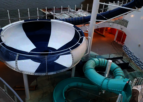 Blau-weiße Body Bowl mit einem transparenten Acrylabschnitt neben einer türkisfarbenen Wasserrutsche auf einem Kreuzfahrtschiff.