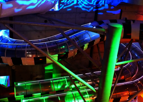 Transparent überdachte Body Racer Rutschen mit blauem und grünem Lichtspiel.