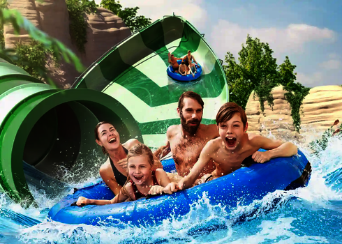 Familie landet auf blauem Rutschreifen lachend im Wasserbecken der Lotus Reifenrutsche.