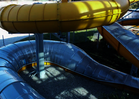 Gelbe und transparente Wasserrutsche, teils auf dem Boden liegend im Außenbereich.