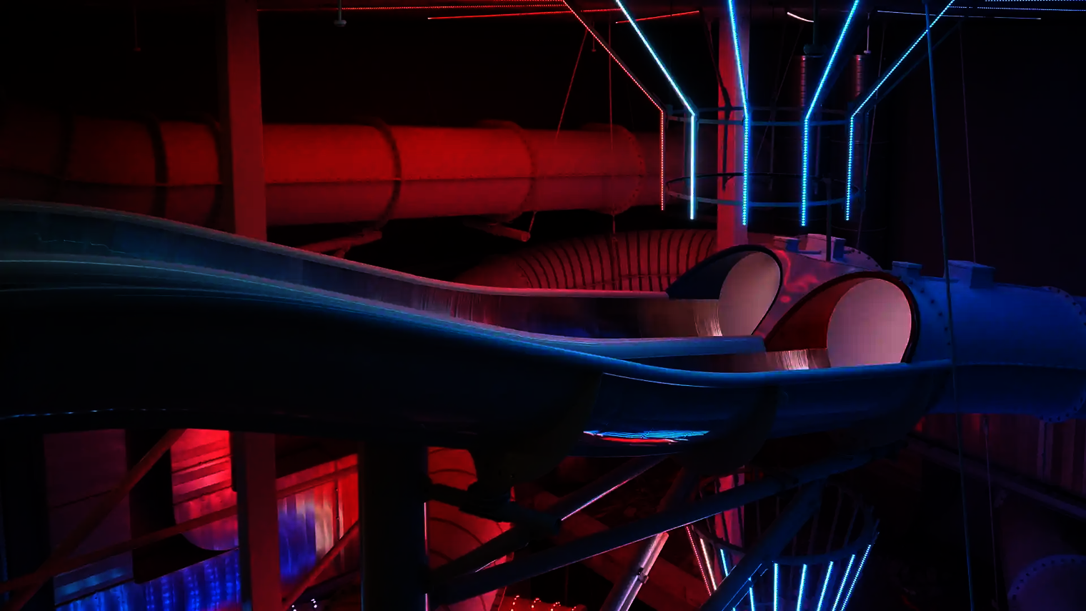 Seitenansicht des Startbereichs der Raft Racer Reifenrutsche mit roter und blauer Röhre bei LED-Beleuchtung.