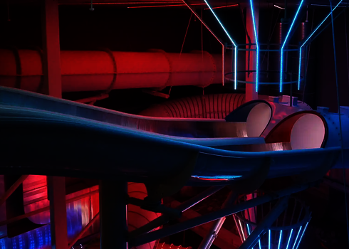 Seitenansicht des Startbereichs der Raft Racer Reifenrutsche mit roter und blauer Röhre bei LED-Beleuchtung.