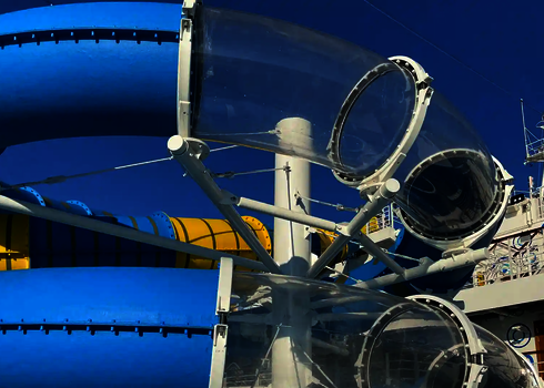 Mehrere transparente Acrylröhren verlaufen zwischen bunten Rutschenteilen auf einem Kreuzfahrtschiff.