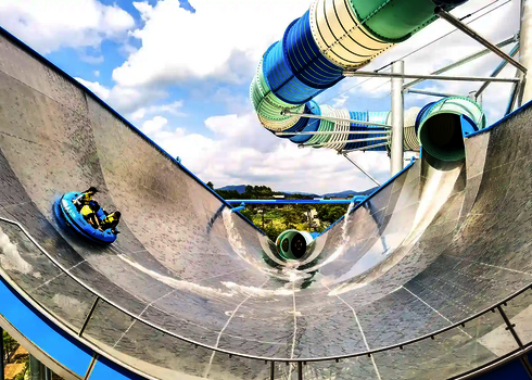 Große Edelstahl Wasserrutsche namens Urknall, im Hintergrund weitere Wasserrutsche in blautönen.