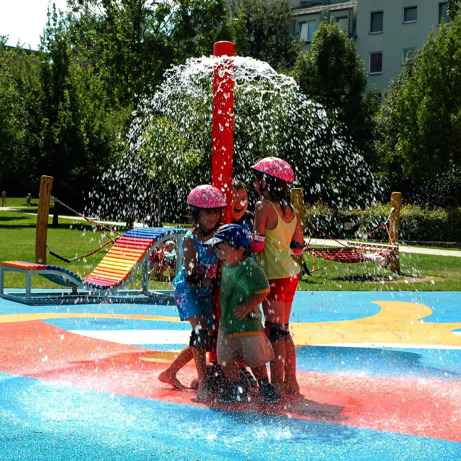 Lachende Kinder auf einem Wasserspielplatz stehen dicht gedrängt am Wie-Spray Element "Spühsäule".