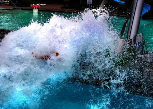 Person befindet sich in großem Wasserschwall über einem Schwimmbecken.