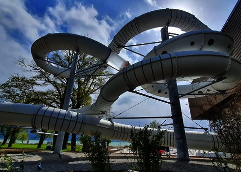 Kurvige Wasserrutsche des Typs RR1400, die außerhalb eines Gebäudes von Stahlstützen getragen wird.