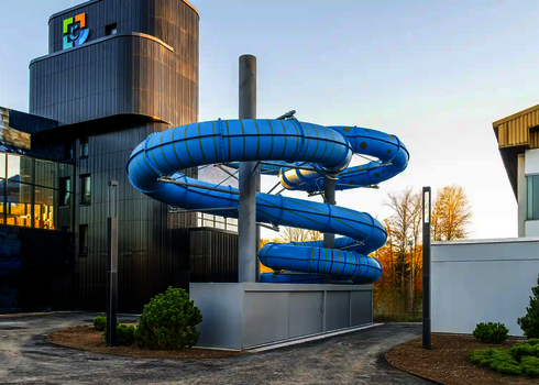 Blick auf eine blaue Wasserrutsche, die spiralförmig außerhalb eines Gebäudes verläuft.