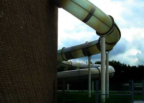 Helle Wasserrutsche mit Streifen verlässt ein rundes Backsteingebäude in Richtung Außenbereich.