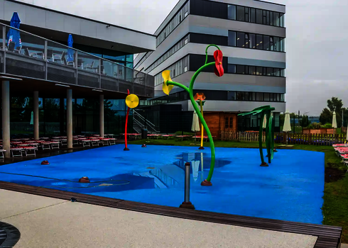 Blauer Kinderbecken mit Wie-Spray Bauteilen vor einer Hotelanlage.