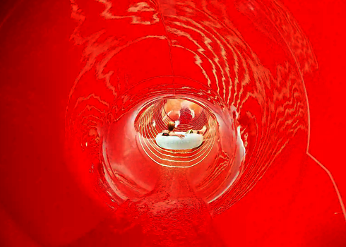 Eine rote Wasserrutsche von innen, im Hintergrund ein roter Rutschreifen.