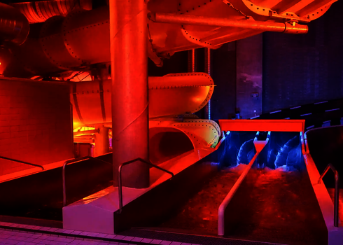 Two illuminated indoor slide chutes with a water channel under coloured lights.