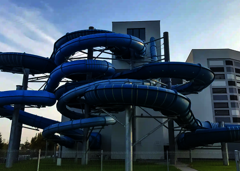 Die verschlungenen blauen Röhren der Family Twister Rutsche winden sich mehrstöckig vor dem Gebäude.