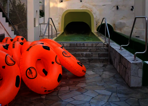 Mehrere orangefarbene Rutschreifen liegen vor dem Einstieg einer dunklen Tunnelrutsche.