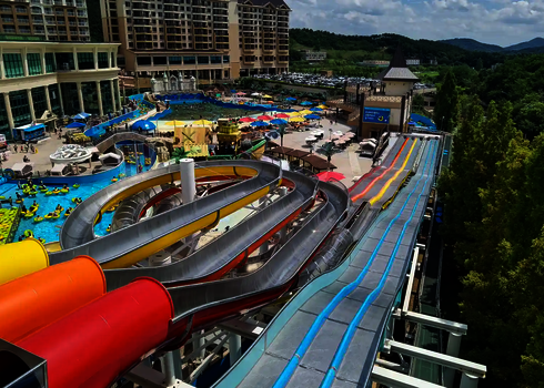 Blick von oben einer Wasserrutsche auf einen Wasserpark, im Hintergrund Hotelgebäude.
