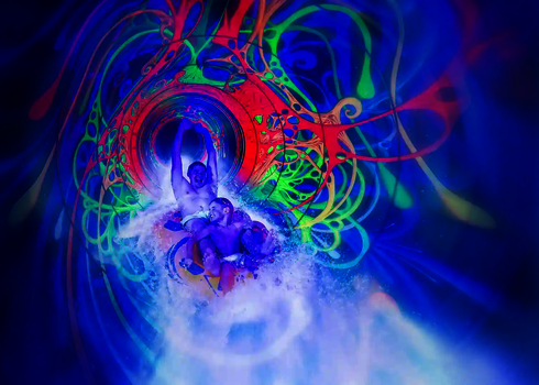 Zwei Personen rutschen durch eine Wasserrutsche mit leuchtenden UV-Mustern in kräftigen Farben.