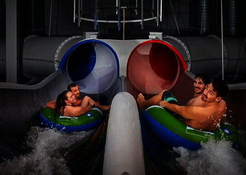 Zwei Teams rutschen parallel in die blau-rote Raft Racer Reifenrutsche mit Wassereinstieg.