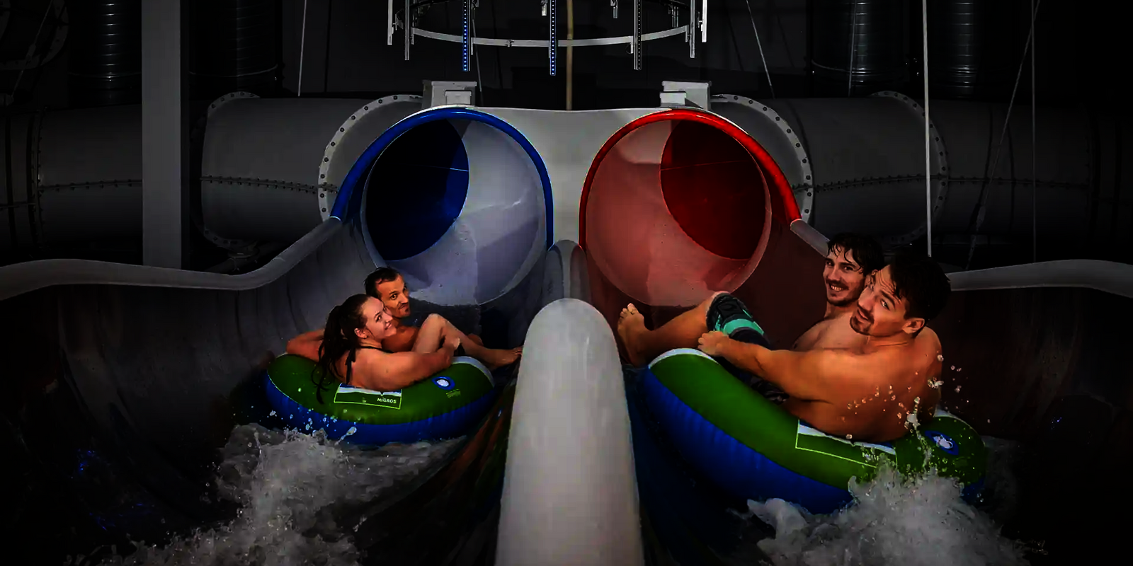 Zwei Teams rutschen parallel in die blau-rote Raft Racer Reifenrutsche mit Wassereinstieg.
