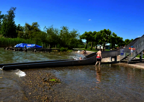 A stainless steel slide leads directly from the shore into a natural lake with a pebble beach.
