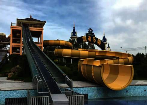 Green raft conveyor runs between yellow slide and slide tower at a water park.