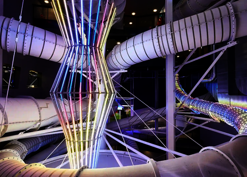 Innenansicht eines Hallenbades mit weißer RR900 Wasserrutsche und bunten LED-Lichtern.