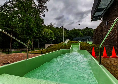Grüner Wildwasserfluss mit leichtem Gefälle neben einem Gebäude.