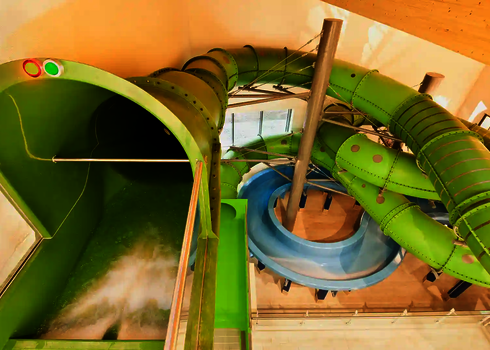 Grüne Wasserrutsche mit rot leuchtender Sensorampel in einem Hallenbad.