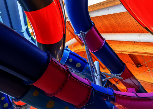 Mehrere farbenfrohe Wasserrutschen mit Punkten und Streifen verlaufen durch eine Halle.