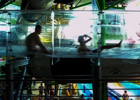 Personen rutschen durch ein mit Wasser gefülltes, transparentes Acryl-Element einer Wasserrutsche.