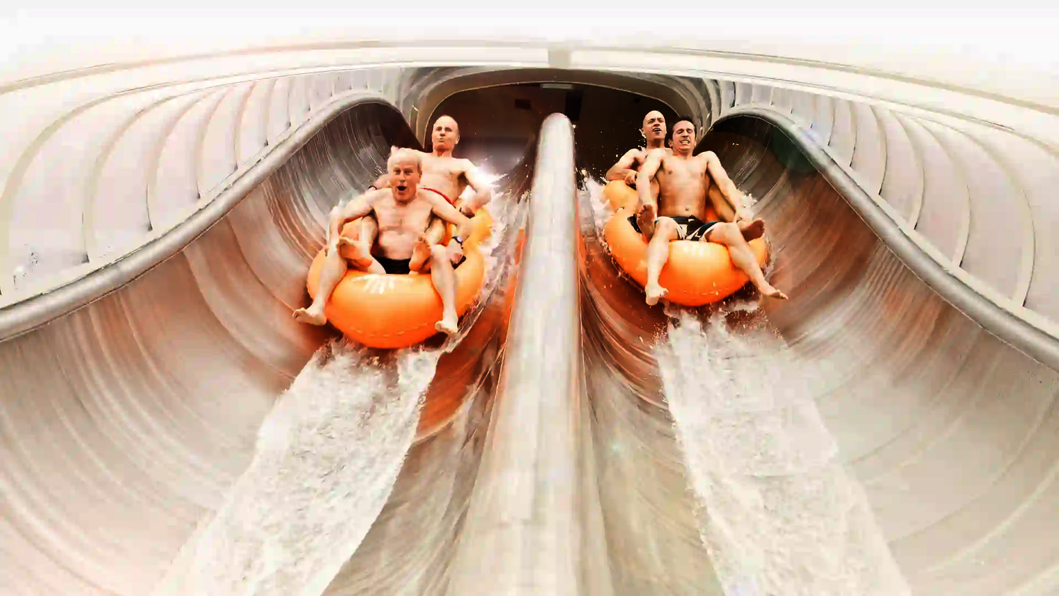 Zwei Teams rutschen parallel in orangefarbenen Reifen auf der Raft Racer Wasserrutsche hinab.