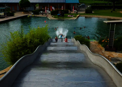 Eine lange Breitwellenrutsche an einem Schwimmbecken an dessen Ende sich einige Badegäste befinden.