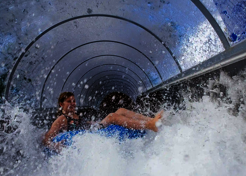 Ein Kind rutscht auf einem Reifen durch den Speed Blaster, Wasser spritzt stark auf.