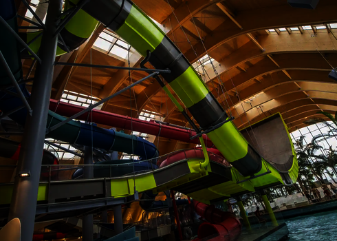 Die Boomerang-Rutsche mit gelb-grauen Elementen verläuft kurvig durch eine Schwimmhalle.