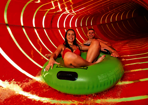 Eine rote Wasserrutsche von innen, mit zwei Frauen auf einem grünen Rutschreifen.