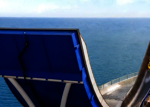 Zwei Personen auf gelbem Rutschreifen rutschen eine Boomerang-Rutsche mit Meeresblick.