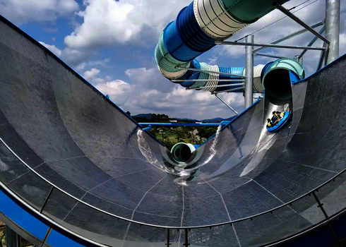 Sehr große Urknall Wasserrutsche aus Edelstahl, auf sich Personen in Rutschreifen befinden.